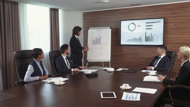 Business meeting, a young businessman speak at a meeting and shows financial infographic in the conference room, man in a suit communicates with colleagues, infographics on tv screen.