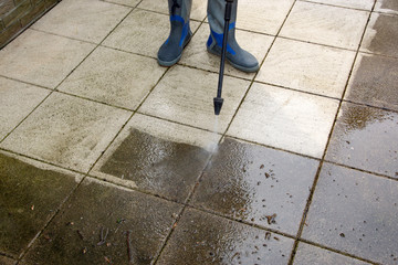 Outdoor floor cleaning with high pressure water jet. Man in rubber boots