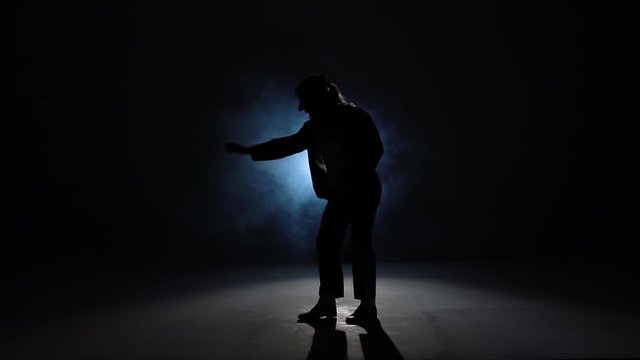 Silhouette of a young man dancer dancing in style Michael Jackson on a blue background of smoke. Close up, slow motion.