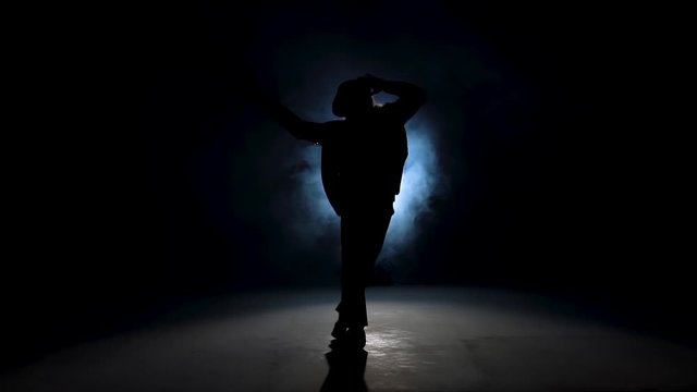 Silhouette of a young man dancer dancing in style Michael Jackson on a blue background of smoke. Close up, slow motion.