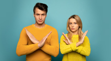 We don’t fancy that. Close-up photo of a perfect couple in yellow outfits, who are looking in the camera, showing their hands crossed as a sign of refusal.