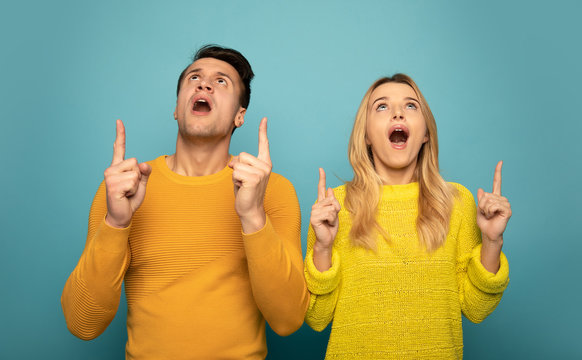 OMG. Top mood. Close-up photo of a magnificent couple in yellow outfits, who are looking up in surprise, pointing upwards with their index fingers.
