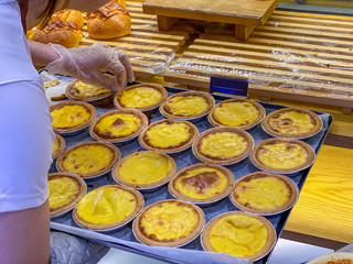 Baker putting fresh golden egg tarts into showcase at bakeshop