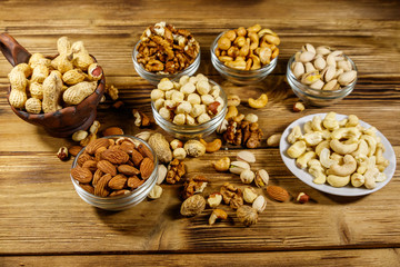 Assortment of nuts on wooden table. Almond, hazelnut, pistachio, peanut, walnut and cashew in small bowls. Healthy eating concept