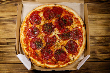 Delicious fresh pizza in cardboard box on a wooden table. Top view. Concept for home delivery of food, fast food, delivery of pizza