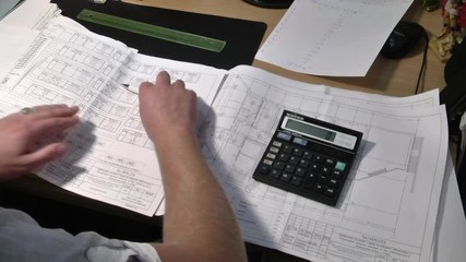 Closeup of human hands drawing architectural plan with pen and calculator. Architect or engineer calculating the plans. Paper electrical engineering drawings. 