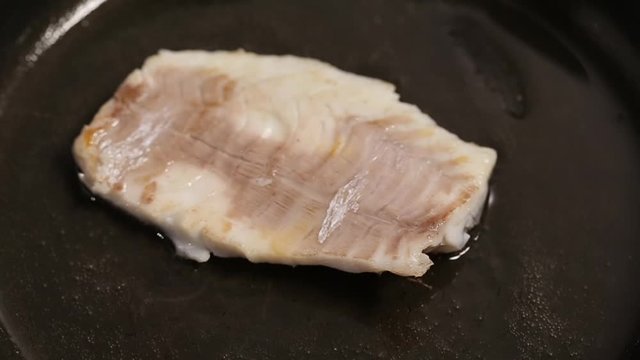 Turning fish fillet on a hot pan with kitchen tongs