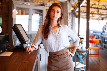 Waist portrait of waitress registrated orders to the payment terminal. Young and beautiful waitress stand near sale terminal and check the order.