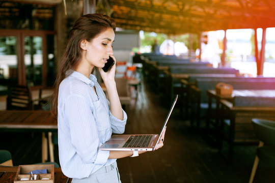 Portrait of female restaurant manager. Businesswoman work with laptop and mobile phone in cafe.