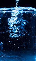 Naklejka na ściany i meble Pour water into glass on black background.