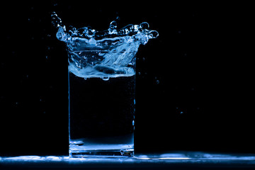 Pour water into glass on black background.