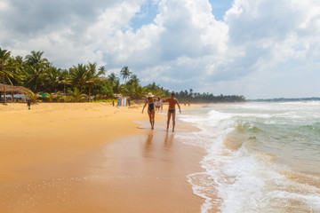 mom and dad lead their little daughter by the hand on the sandy shore of tropical beach in Sri Lanka.