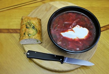 Ceramic plate red borscht white sour cream bread with parsley and garlic folding knife wood background