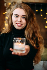 Girl dressed in black clothes holding a glass with a candle in the hands.