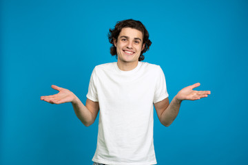 Front view of smiling young man showing shrug gesture isolated on blue background