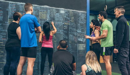 Athlete woman writing down results on the gym blackboard with her classmates and coach