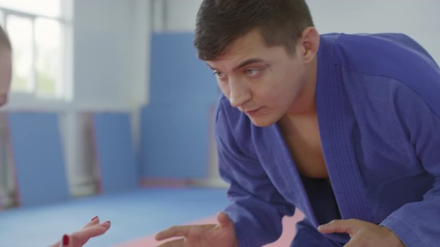 Sequence of shots of male and female opponents in Jiu jitsu gi standing in ready stance, greeting each other and then practicing fight in gym