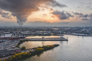 Aerial drone view of Port of Hamburg during sunset with smoke and heavy clouds over the shipyards by the sea