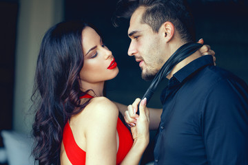 Tempting milf woman in red holding young lover by tie