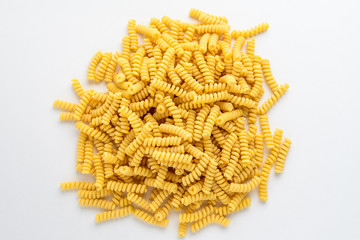 Dried fusilli Italian pasta displayed randomly on a white table, ready to be cooked, isolated on white background, side view of healthy food 
