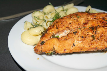Chicken breast fried with spices and boiled pasta with herbs on a white plate.