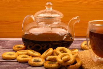Bagels, a glass of tea and a glass teapot of tea on a wooden background.