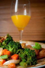 Sauteed fresh vegetables accompanied by a glass of orange juice, beautifully presented on a luxurious plate on a wooden table.