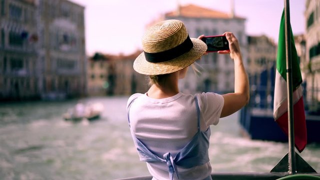 Happy smiling female traveller floating on touristic boat around Venice city making video for creating publication in social network with information about italian trip during summer holidays