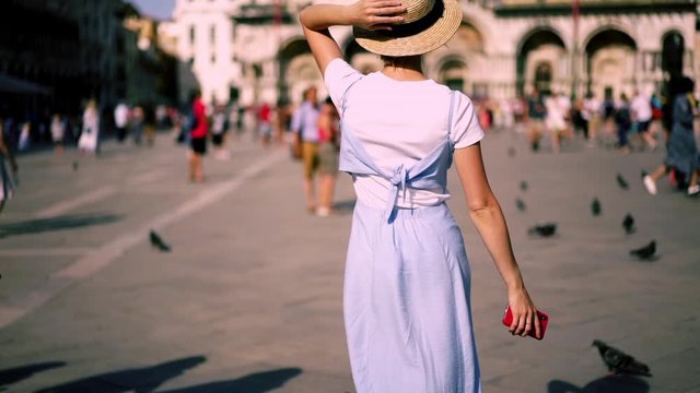 Slow motion effect of excited carefree female traveller in stylish blue sundress walking around famous San Marco Square and enjoying sunny day during Italian vacations in Venice. Touristic destination