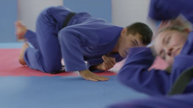 Tilt down of professional male and female fighters in kimonos practicing jiu-jitsu together in gym during partner workout
