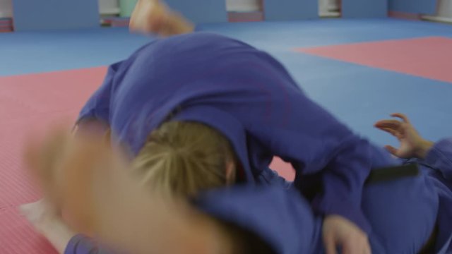 Sequence of shots of male and female jujutsu athletes doing lockdowns and chokeholds during sparring fight on mat in martial arts gym