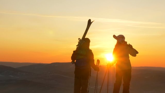 A couple of mountain skiers in love stands on the slope of the mountain and admires the sunset