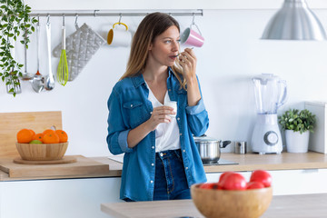 Pretty young woman eating yogurt while standing in the kitchen at home.