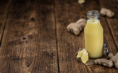 Old wooden table with fresh Ginger Juice (close-up shot; selective focus)