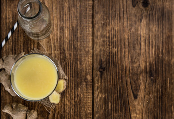 Old wooden table with fresh Ginger Juice (close-up shot; selective focus)