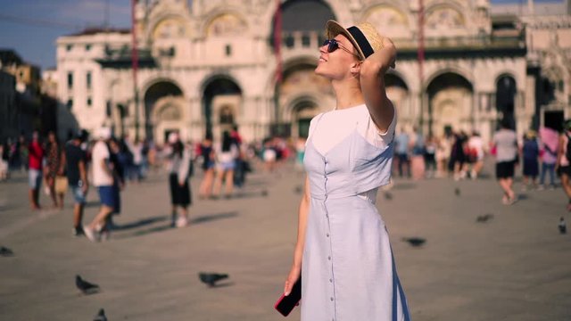 Slow motion of happy smiling female tourist exploring San Marco Square with smartphone in hand and taking photo of Venice showplaces for share publication on travel blog. Touristic summer destination