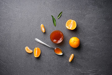 Fototapeta na wymiar Tangerine jam with tangerines and green leaves on a dark background flat lay.