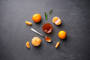 Fototapeta na wymiar Tangerine jam with tangerines and green leaves on a dark background flat lay.