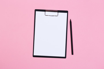 Clipboard with white sheet and pen on a pastel pink background. View from above. space for text