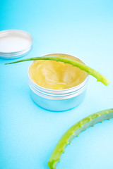 Top view of aloe vera leaf and container with organic moisturizing cosmetic cream on the blue background.