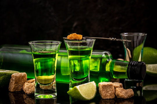 absinthe shots with sugar cubes. absinthe poured into a glass. bottle of absinthe with brown sugar and lime isolated on black background
