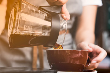 Barista pouring black coffee into a red cup.
