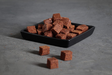 Dessert chocolate cookies cut into cubes, with coffee on a dark gray background