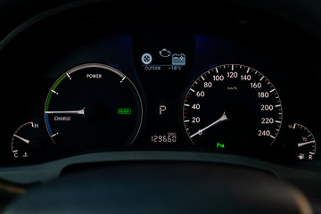 The dashboard of  car is glowing white with arrows at night with a speedometer, charge battery level and other tools to monitor the condition of the hybrid vehicle in modern style on black background