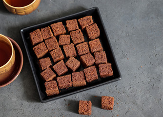 Dessert chocolate cookies cut into cubes, with coffee on a dark gray background