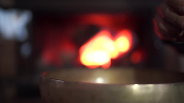 Una mano  toca h&aacute;bilmente un cuenco tibetano. Contra un tel&oacute;n de fondo de llamas de fuego  danzantes 