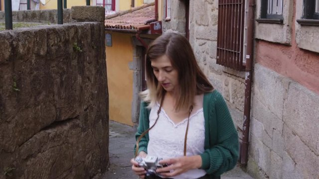 Young woman, traveler is walking in old European town, Porto, Portugal, taking photos on vintage camera, admiring city views, enjoying her vacations, in a good mood.