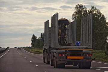 Naklejka na ściany i meble Empty wood truck drive with a trailer on a suburban asphalt highway road on summer evening, timber transport, forestry business