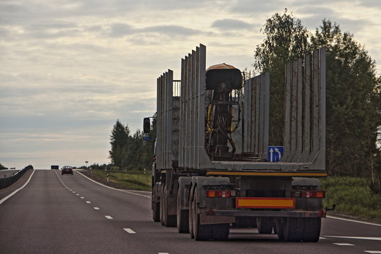 Empty Wood Truck Drive With A Trailer On A Suburban Asphalt Highway Road On Summer Evening, Timber Transport, Forestry Business