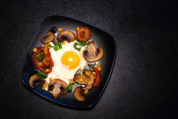 Freshly fried scrambled eggs with vegetables on a black plate